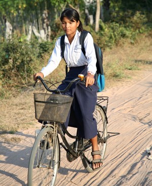 Une jeune fille appareillée avec une prothèse fait du vélo sur une route en terre