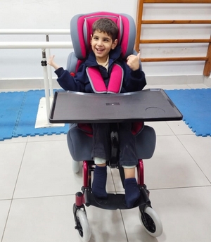 Jeune garçon souriant dans un fauteuil adapté à son handicap.