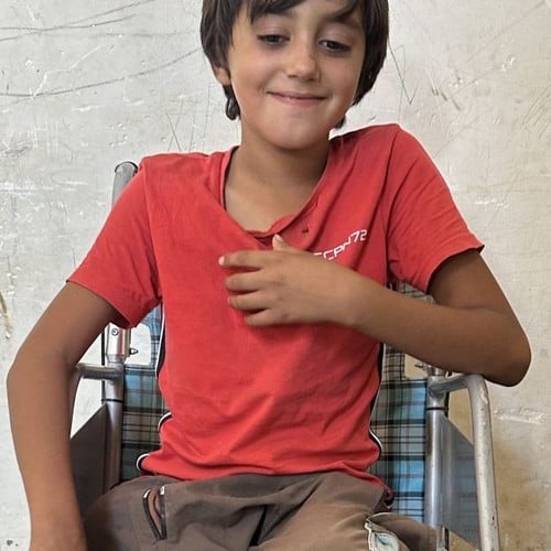 Un jeune garçon syrien souriant est assis dans un fauteuil roulant.