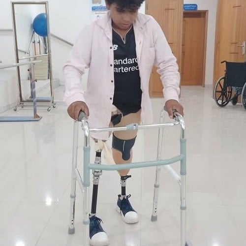 Un jeune garçon appareillé des deux jambes se tient debout à l'aide d'un déambulateur.