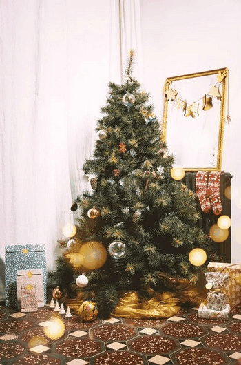 Un Sac à Sapin de Handicap International emballe un sapin dans un salon, pendant les fêtes de Noël. Des cadeaux et décorations de fêtes se trouvent autour.