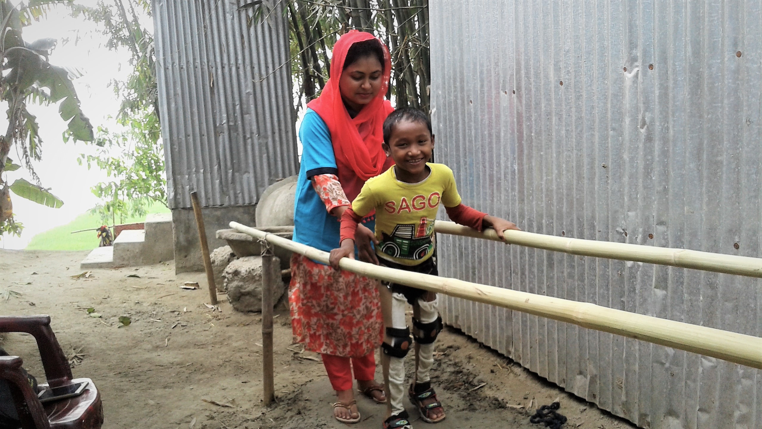 Enfant équipé de prothèses faisant des exercices de marche au Bangladesh avec des barres parallèles en bambou.