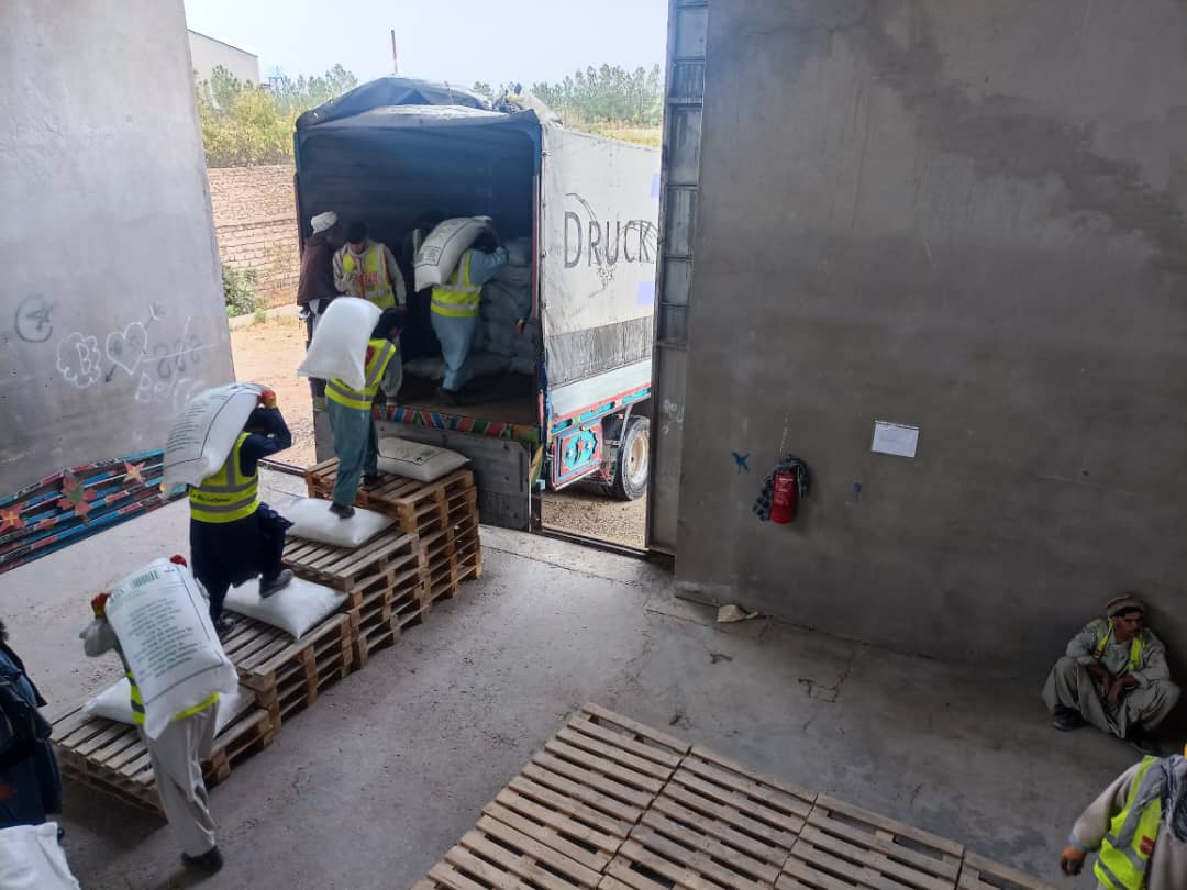 Dans un entrepôt, plusieurs hommes déplacent des sacs dans un camion garé devant le quai de chargement.