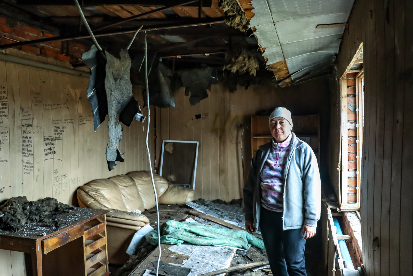 Une femme chaudement vêtue se tient debout dans une pièce de sa maison en Ukraine qui a été en partie détruite.