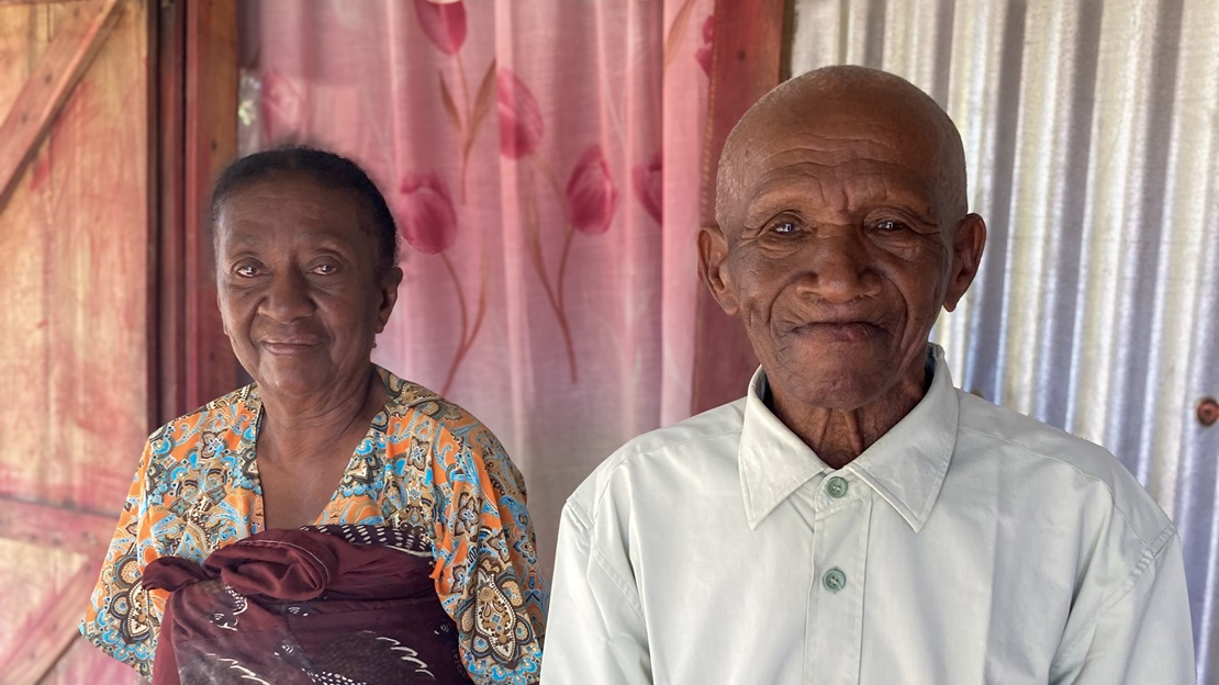 Un couple de personnes âgées pose devant sa maison.