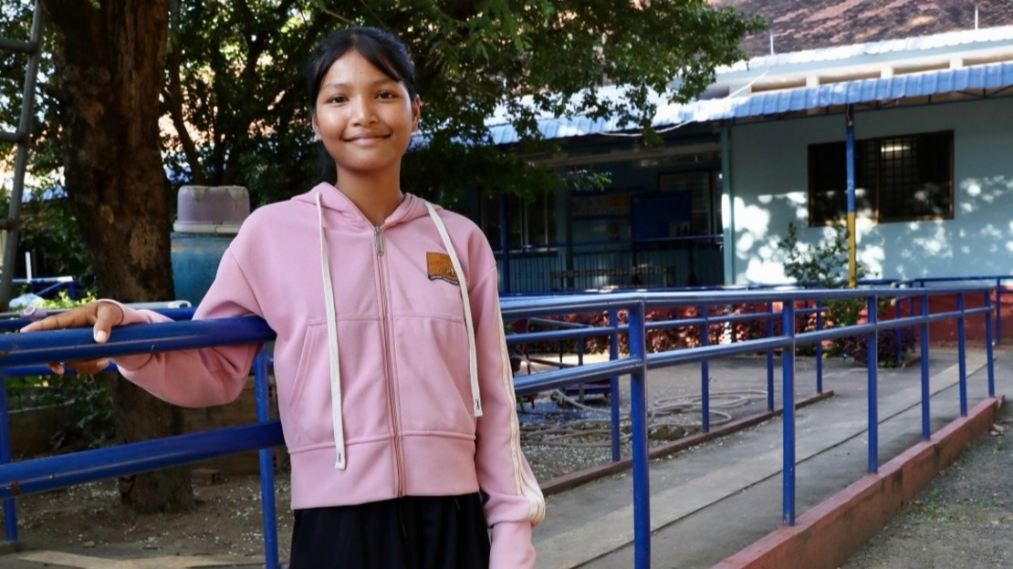 Une jeune Cambodgienne est adossée à une barre d'exercice de kinésithérapie dans la cour d'un centre de réadaptation.