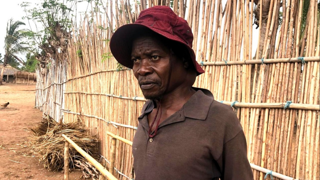 Portrait en gros plan d'un homme qui regarde sur la gauche. Il s'accoude à deux barres de bois parallèles, une installation destinée à la réalisation d'exercices de rééducation.