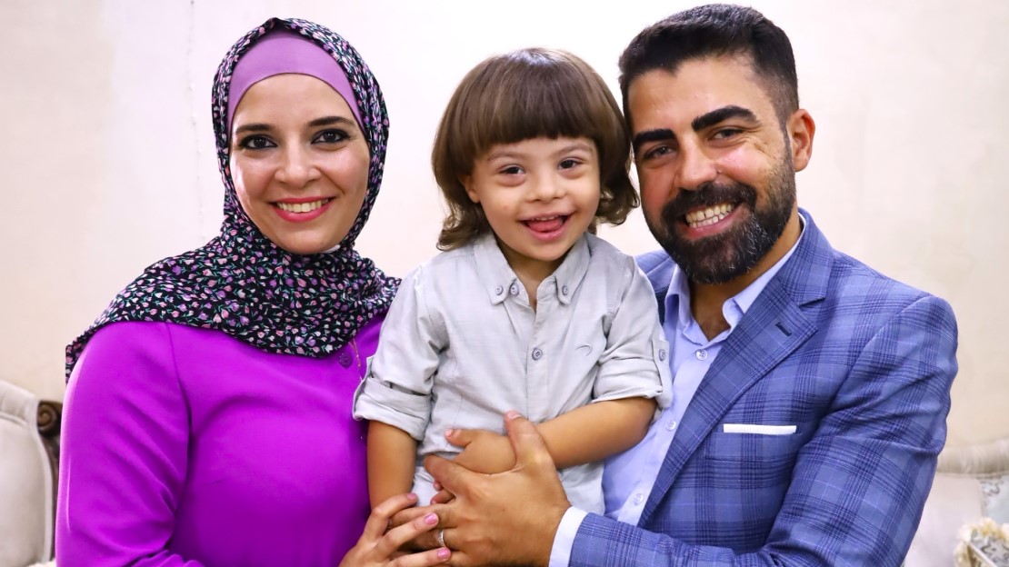 Un couple pose avec son enfant dans les bras de son père. Tous les trois sourient.