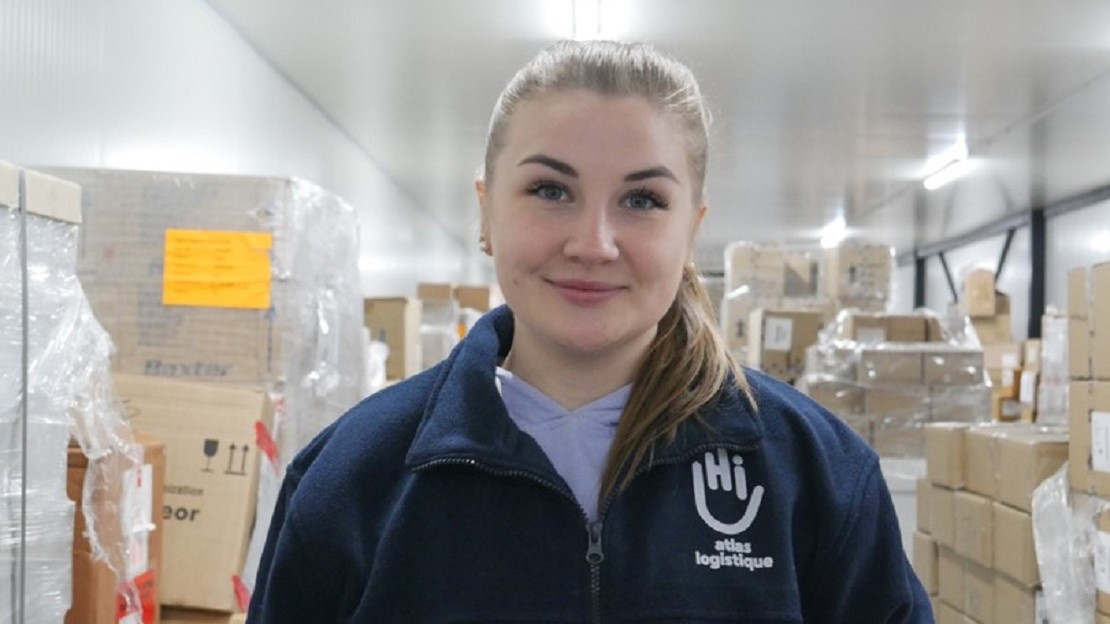 Dans un entrepôt, portrait d'une jeune femme qui porte un pull HI.