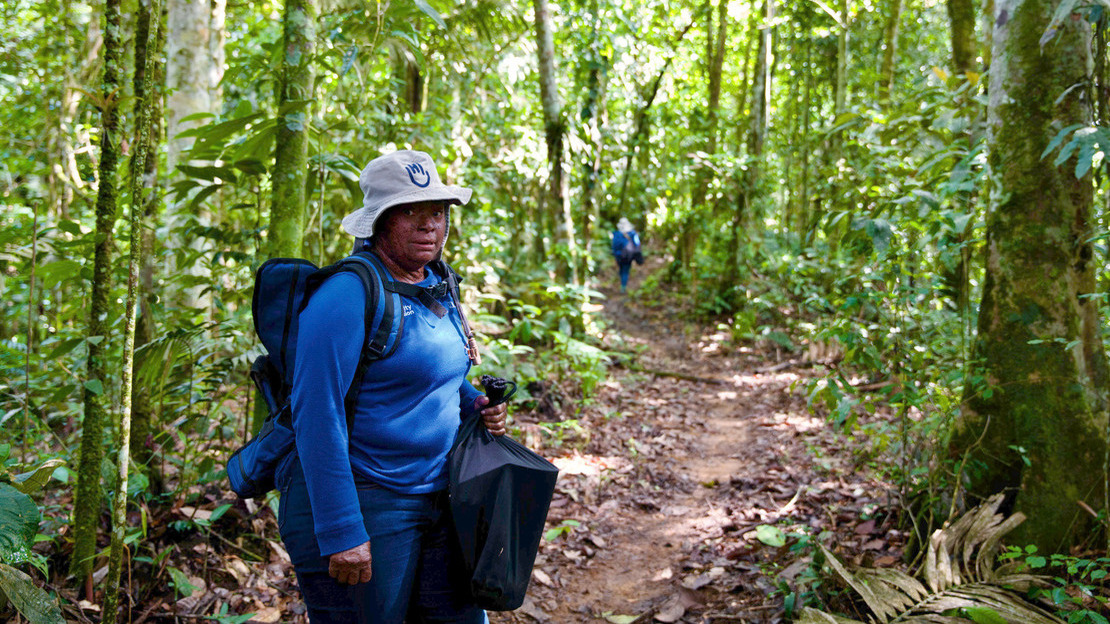 Portrait d'une femme debout sur une route de terre au milieu d'une forêt à la végétation luxuriante.