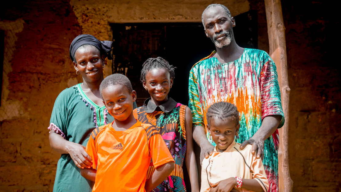 Portrait de famille, devant la maison familiale construite en briques rouges. Les parents et les trois enfants sourient au photographe.