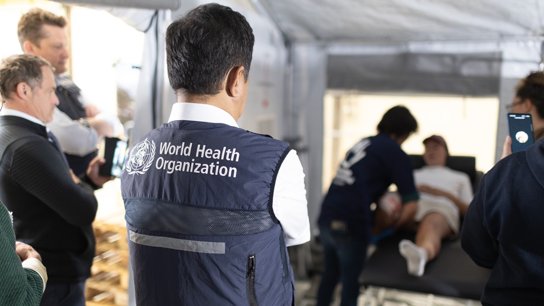 De dos, un représentant de l'Organisation Mondiale de la Santé observe un exercice de mise en situation de soins de réadaptation d'urgence par une équipe de Handicap International / Humanity & Inclusion.