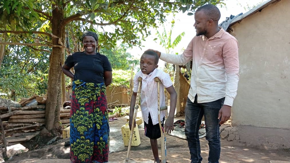 Salama, un jeune homme en Ouganda, se tient debout au centre de l'image avec ses deux béquilles.