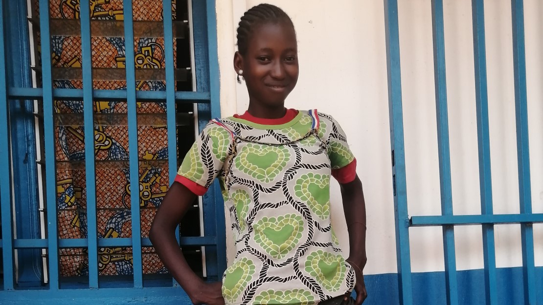 Une adolescente se tient debout devant une salle de réadaptation. Elle sourit en montrant sa prothèse.