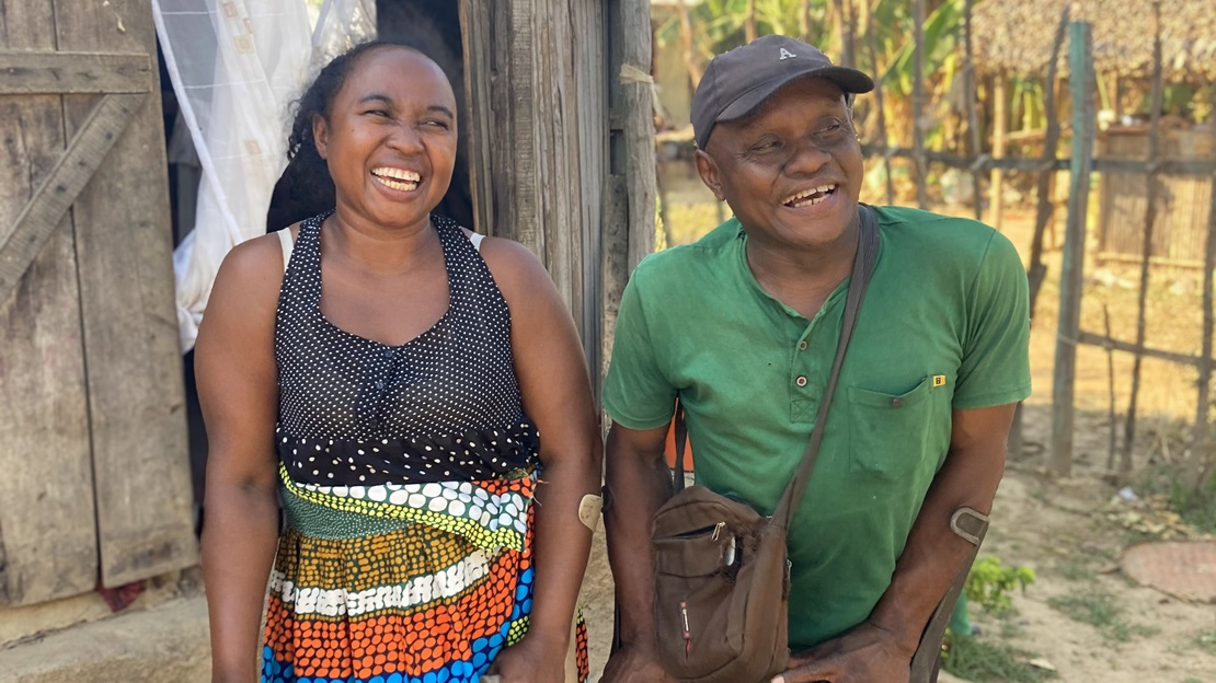 À Madagascar, une jeune femme et un homme handicapé se tiennent debout devant une maison et sourient.