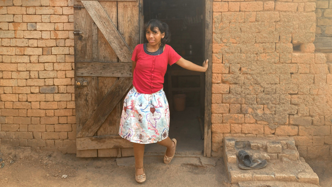 Fifaliana est debout devant une porte, en extérieur. Elle sourit et porte une jupe, et a une prothèse à la jambe droite.