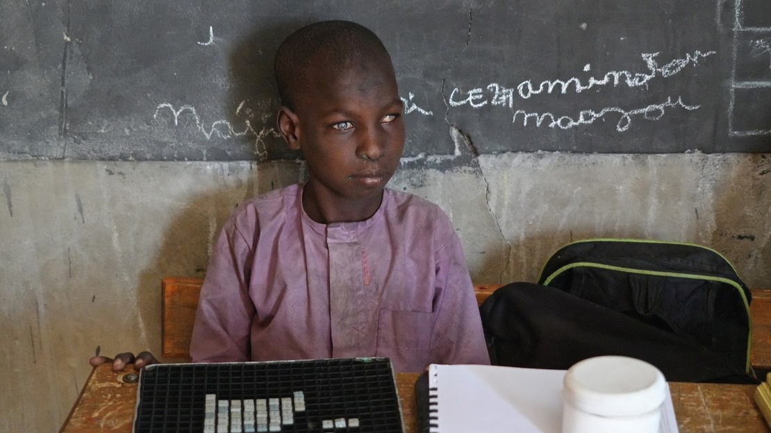 Photo de Souleymane, 13 ans, en classe au Niger. Il est assis devant un tableau noir, face à un bureau.