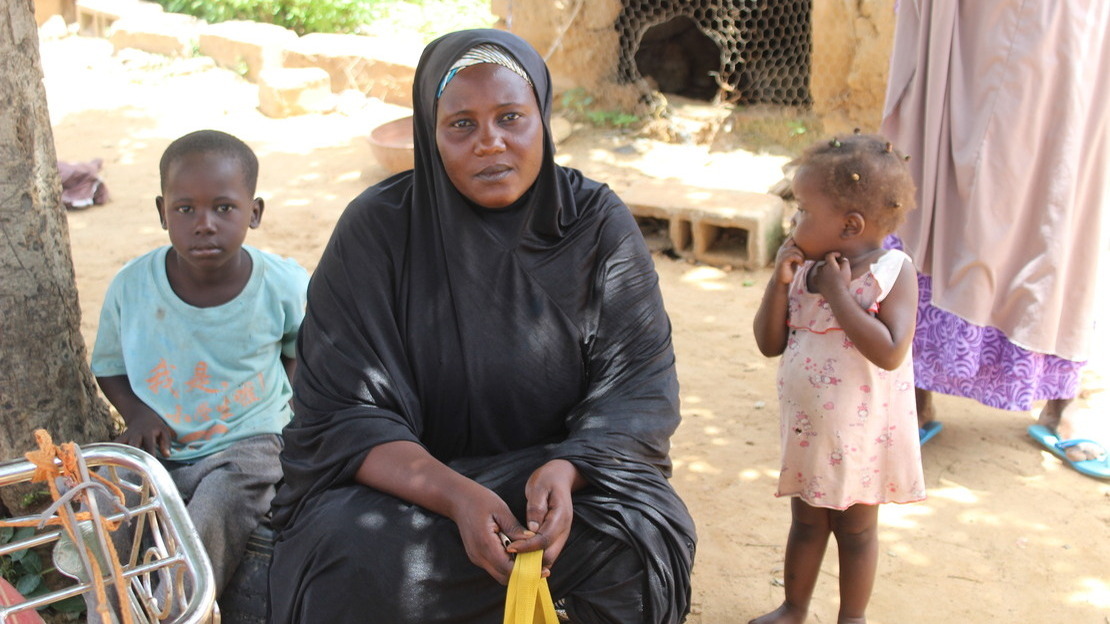 Portrait d'une femme et de deux enfants, assis dans une cour de terre battue. La femme et le garçon regardent la caméra.