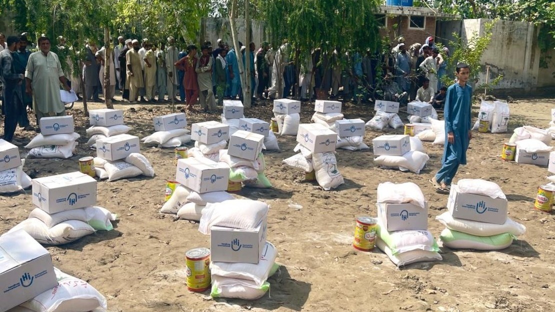 Au Pakistan, des provisions alimentaires préparées par Handicap International sont posées sur le sol alors que les bénéficiaires font la queue pour recevoir leurs kits.