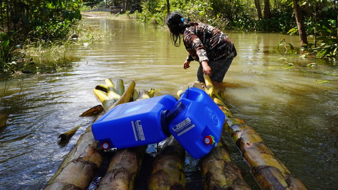 Une femme doit traverser les terrains inondés pour rejoindre sa maison avec les bidons d’eau et les kits d’hygiène fournis par HI dans le cadre de sa réponse d’urgence. 500 ménages touchés par les inondations ont déjà reçu le soutien de HI, dans la province de Davao del Norte.