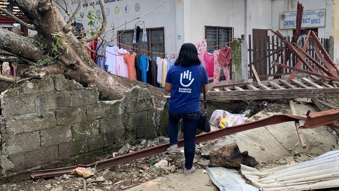 Une employée de Handicap International se tient debout au milieu des ruines d'une maison détruite par un typhon aux Philippines.