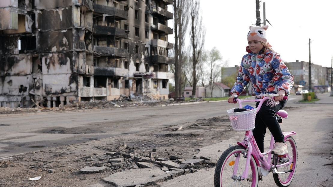 Une petite fille fait du vélo devant des immeubles détruits par les bombardements à Borodyanka, en Ukraine
