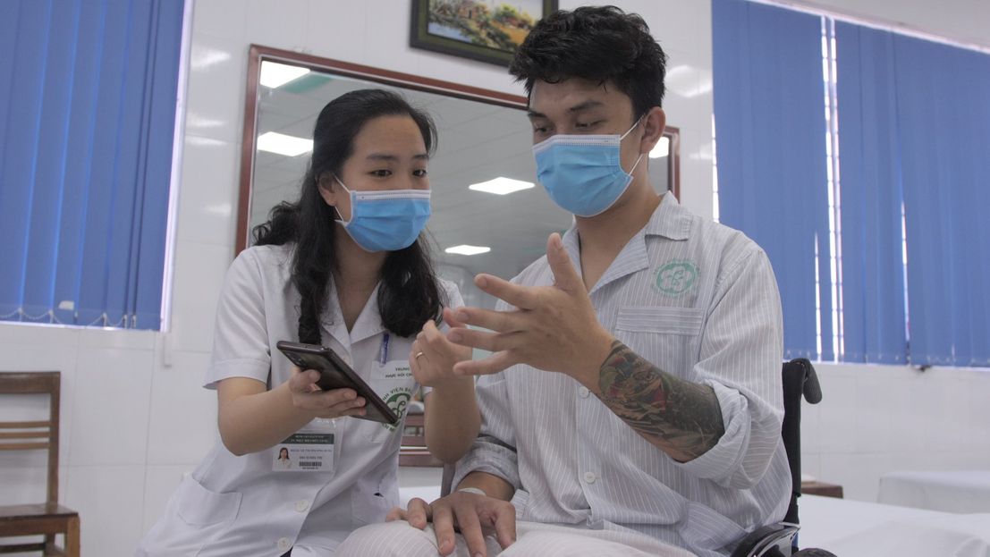 Une professionnelle de la réadaptation montre à un patient comment utiliser l'application mobile OpenTeleRehab au Vietnam.