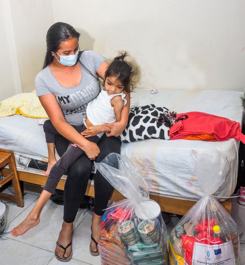 Luisa portant sa fille Alicia et les paniers d'aliments donnés par Handicap International