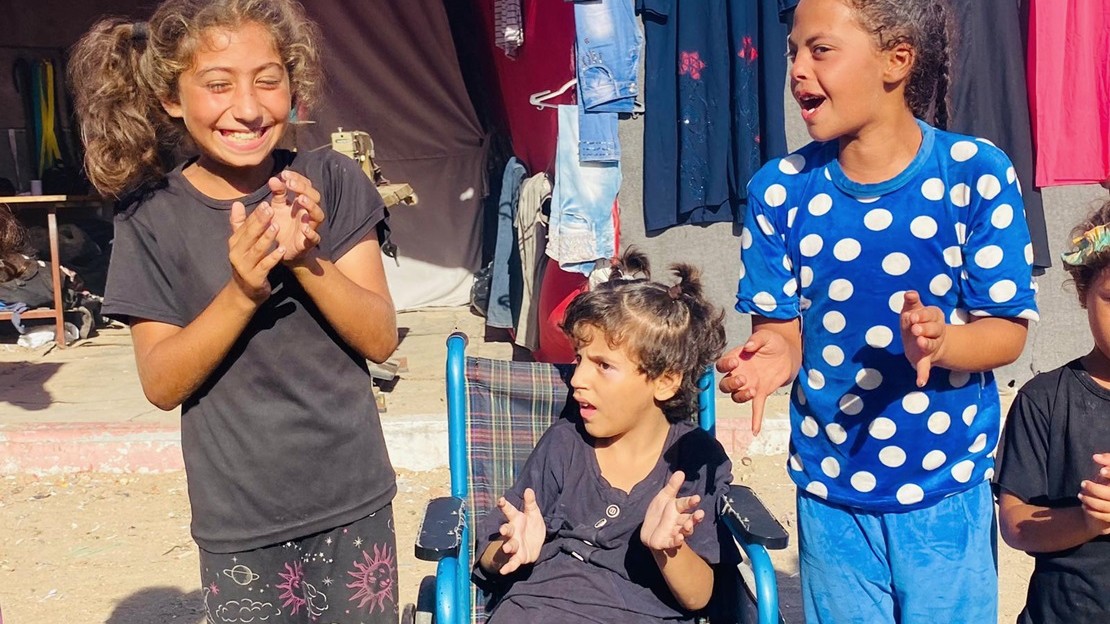 Trois jeunes filles sont en train de taper dans les mains lors d'une activité récréative. Celle du milieu est dans un fauteuil roulant.