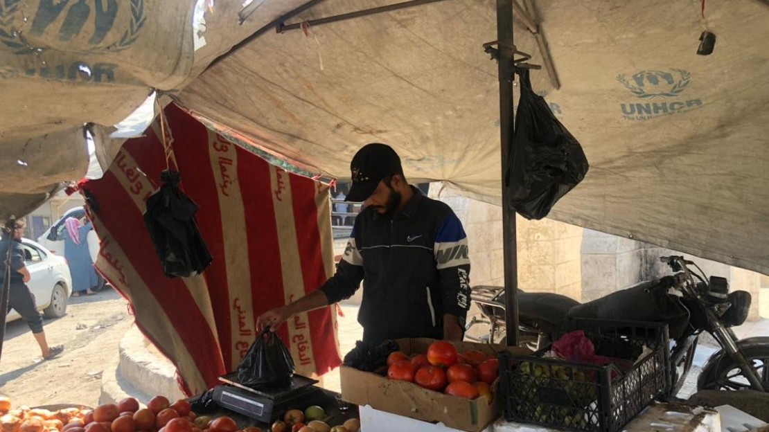 Un homme se tient debout devant un étal au marché et pèse des fruits.