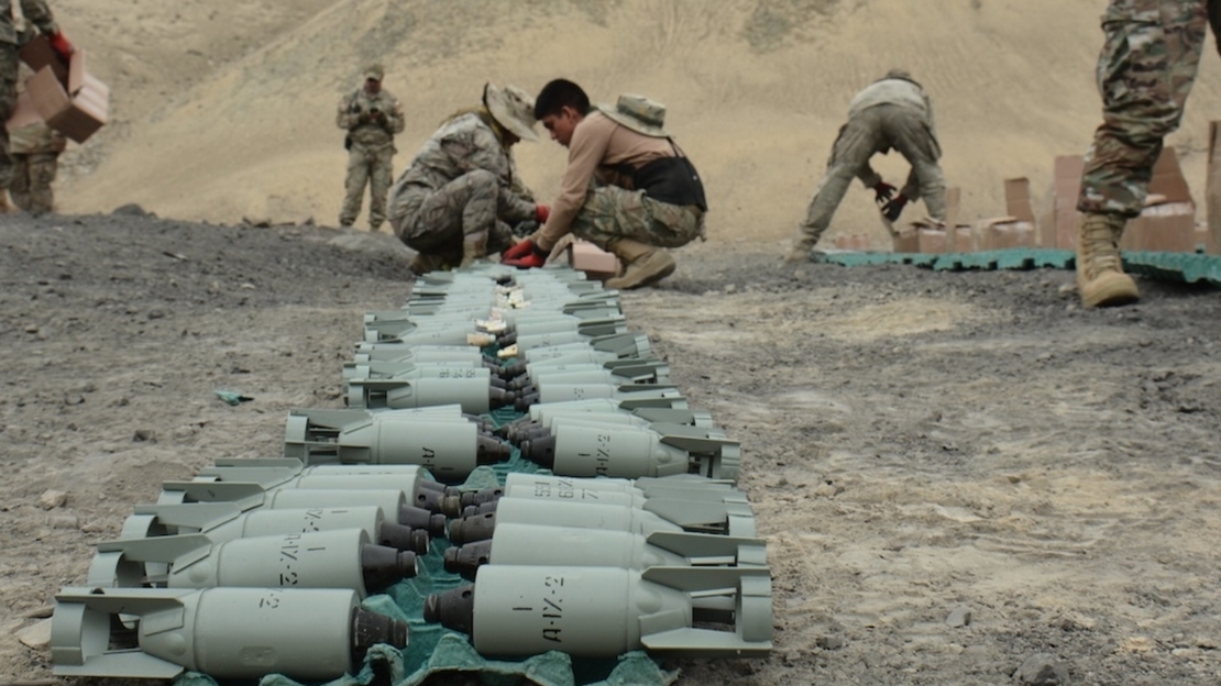 Des personnes habilitées manipulent des bombes à sous-munitions dans un terrain dégagé.