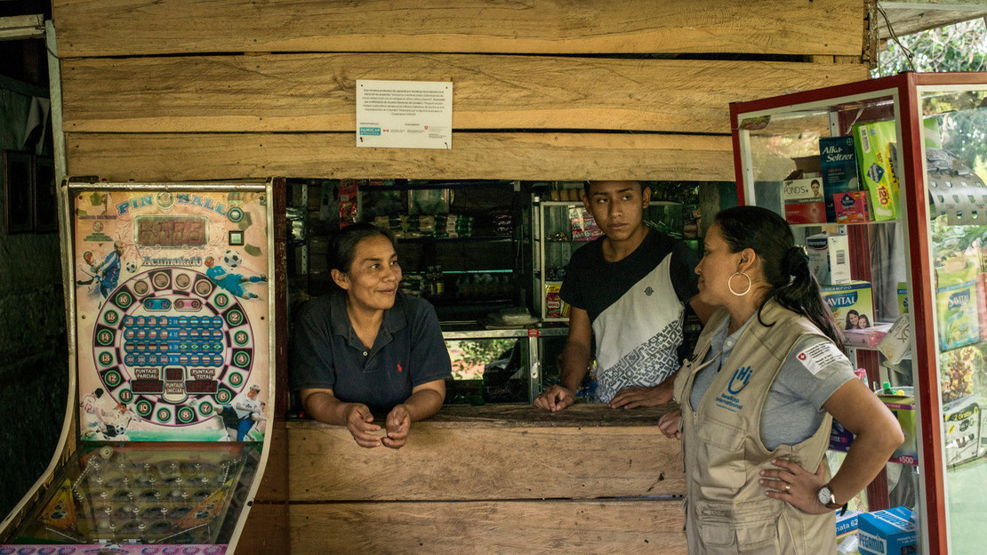 Une femme portant une jaquette HI discute avec une femme et un homme qui se tiennent derrière un comptoir en bois.