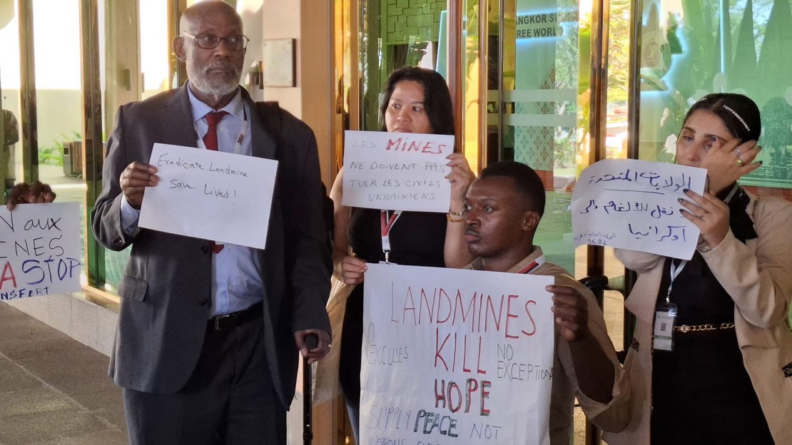 Deux femmes et deux hommes tiennent dans leurs mains des affiches avec des messages en plusieurs langues sur le combat contre les mines antipersonnel.