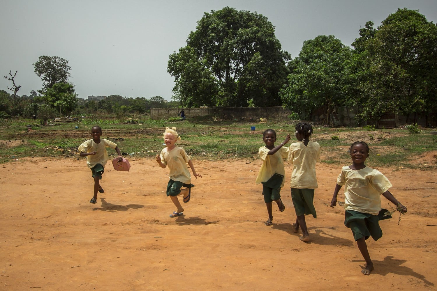 Sur un terrain en Afrique, des enfants courent. Parmi eux, une fillette atteinte d'albinisme.