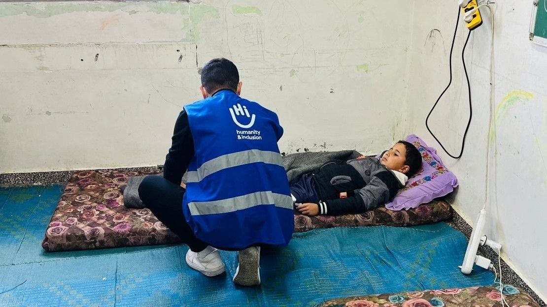 Un jeune garçon est allongé sur un matelas dans une pièce. Au premier plan, un professionnel de la santé est accroupi à côté de lui et lui prodigue des soins.