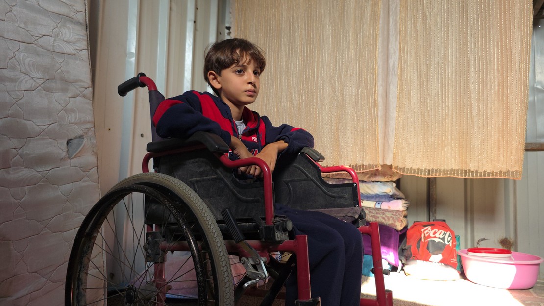 Un jeune garçon en fauteuil roulant regarde au loin avec un air triste.