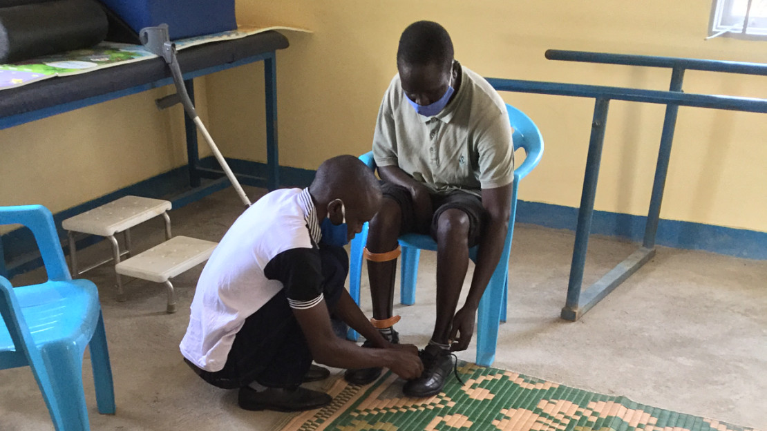Hakim avec le collaborateur de Handicap International pendant l’essai de son appareillage de jambe fabriqué par impression 3D, dans le camp d’Omugo en Ouganda