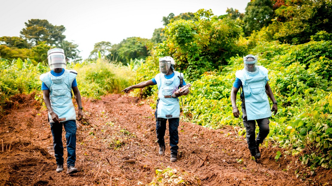 Trois démineurs de Handicap International équipés de leur tenue de protection marchent dans un corridor et font des repérages avant de se mettre au travail.