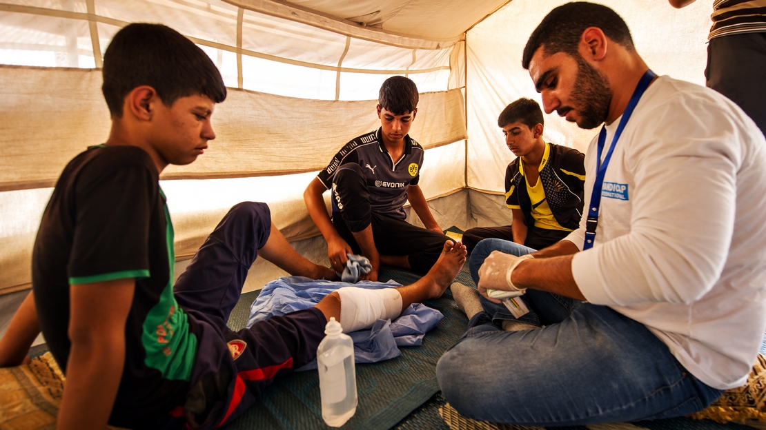 Dans un camp de déplacés en Irak, un kiné de Handicap International avec un enfant originaire de Mossoul, blessé par un éclat d'obus qui a causé une fracture de sa jambe. La kinésithérapie permet de restaurer sa mobilité.
