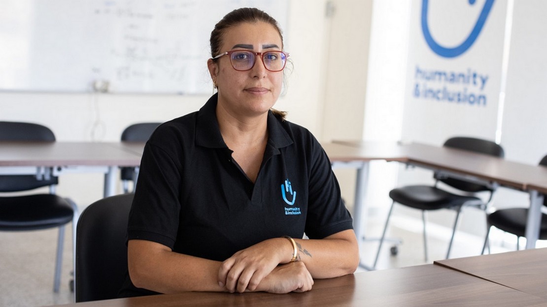 Une femme est assise à un bureau, les bras croisés, et regarde le photographe.
