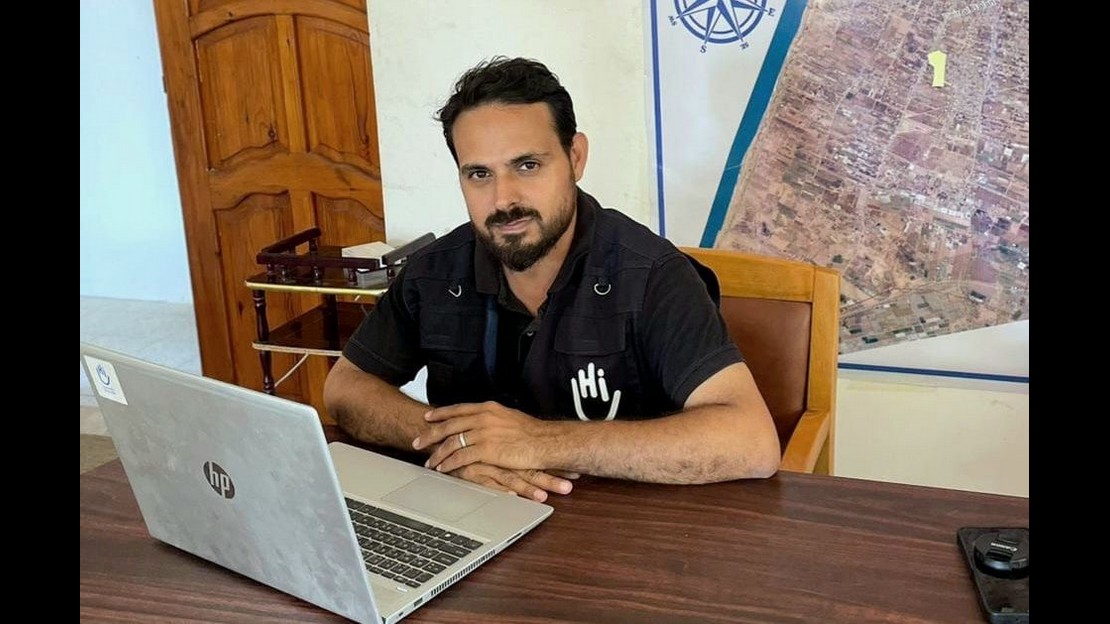 Un homme assis à son bureau devant son ordinateur portable regarde le photographe.