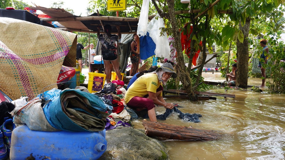 Aux Philippines, une femme lave des habits dans le fleuve à coté d'un abri de fortune après le passage d'une tempête tropicale.