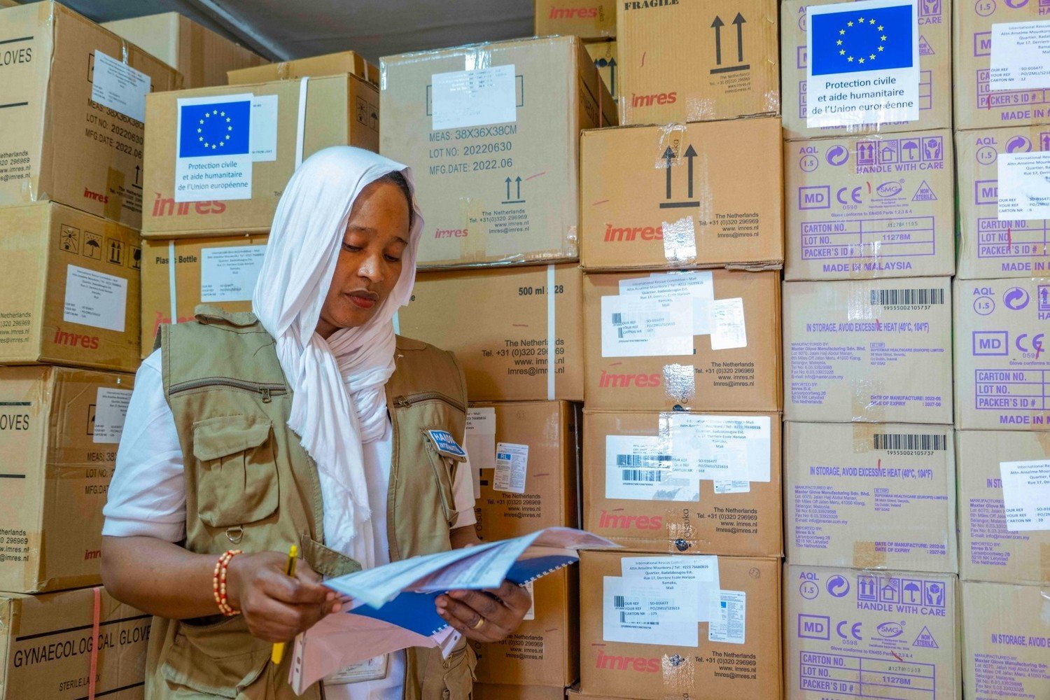 Une femme debout lit des fiches devant des dizaines de cartons empilés.