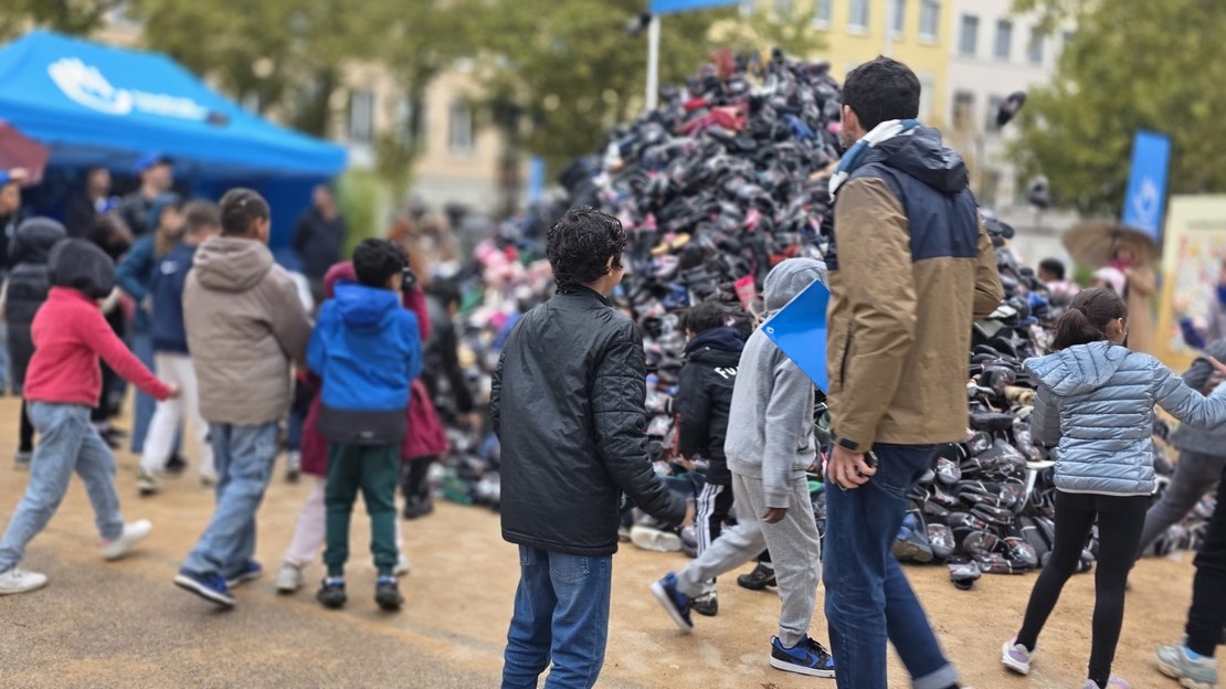 Plusieurs personnes de dos, surtout des jeunes, devant la Pyramide de chaussures de Handicap International à Lyon.