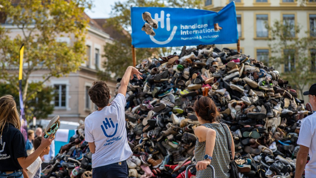 Devant une pyramide de chaussures, plusieurs personnes lancent des chaussures dans sa direction.
