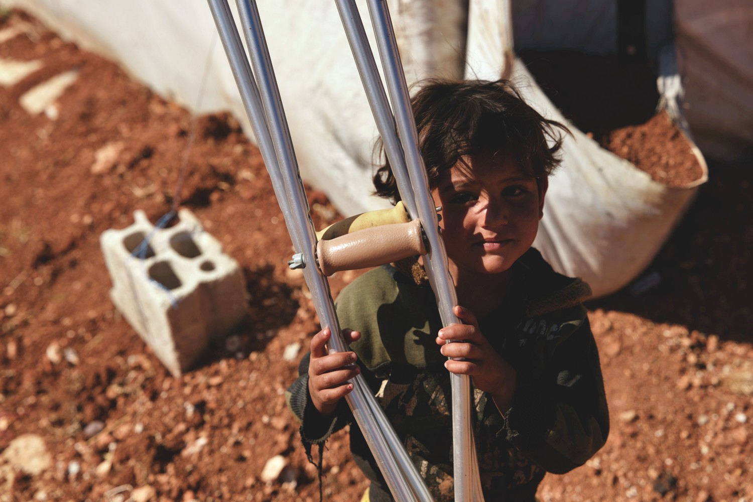 En Syrie, un jeune garçon tient une paire de béquilles et sourit au photographe.