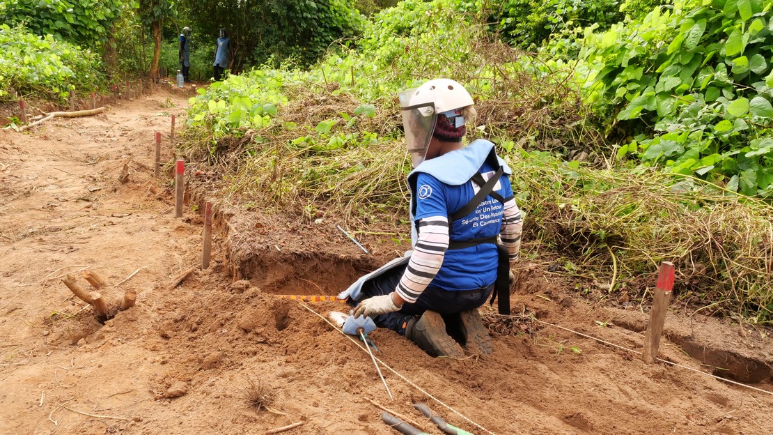 Au Sénégal, une démineuse est en train de travailler accroupie au sol devant une tranchée dans la terre.