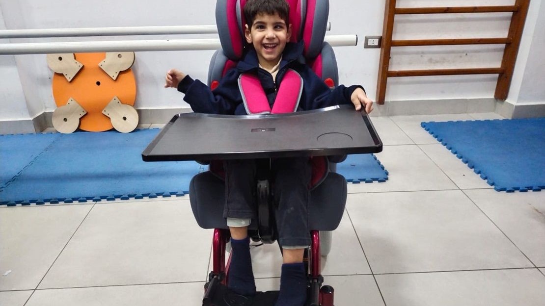 Dans une salle de rééducation, un jeune garçon dans son fauteuil roulant sourit au photographe.