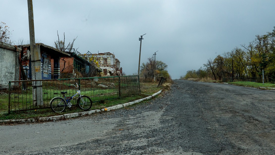 Zone dépeuplée en Ukraine montrant une route, un vélo posé le long d'une barrière, des habitations qui semblent vides et, au dernier plan, un immeuble portant des traces d'impacts d'armes ou de bombardements.