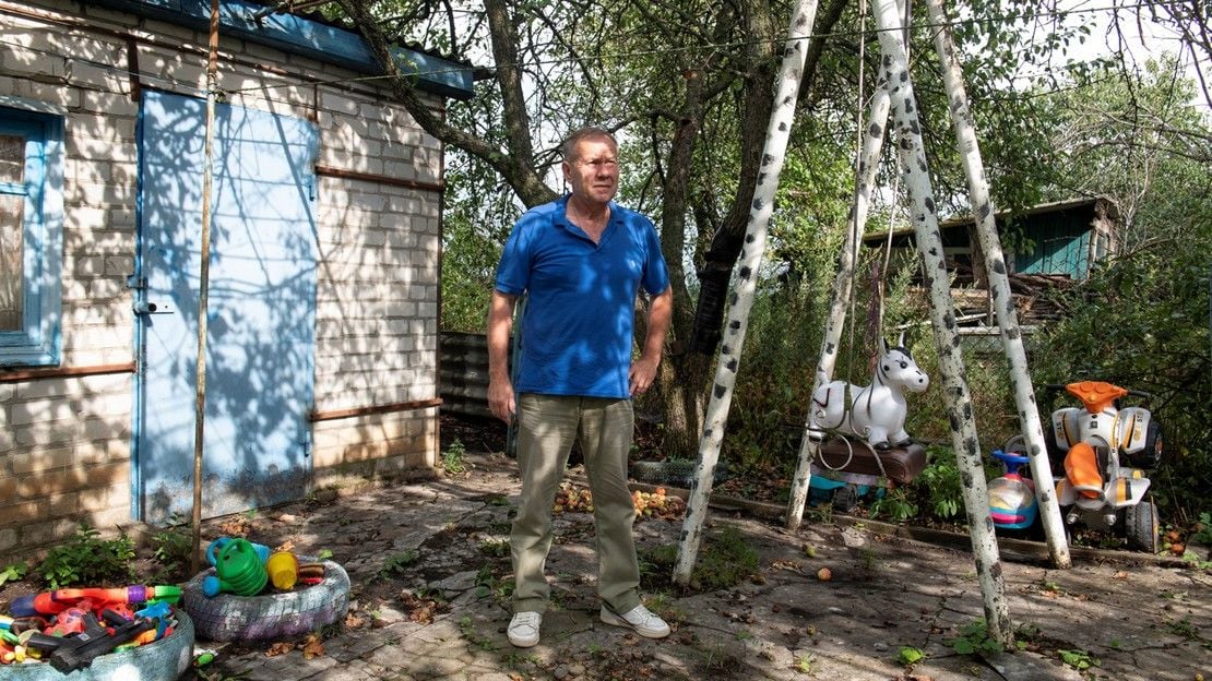 Un homme pose debout dans son jardin.